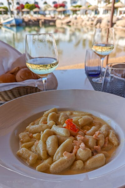 white china plate of gnocchi with a dollop of orange salmon roe in the centre on a table with a lake in the background