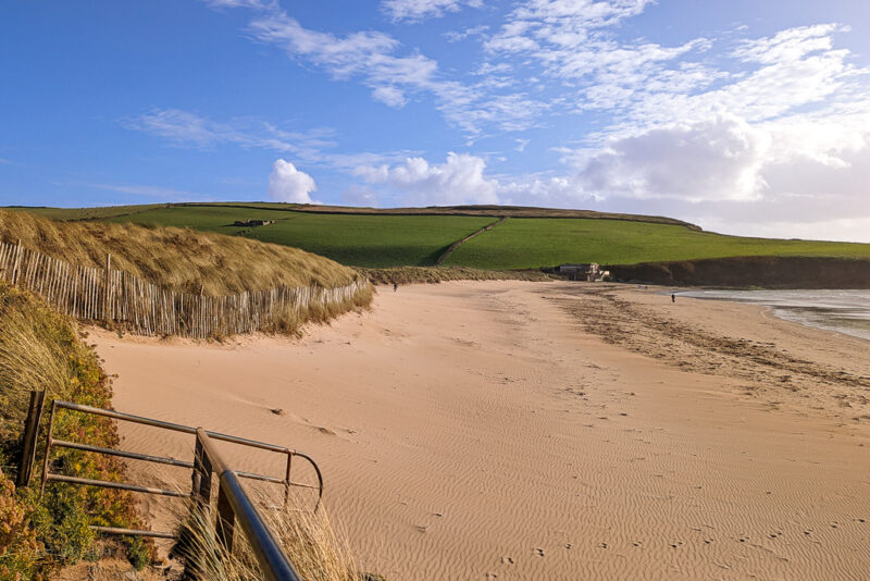 flat, empty sandy beach with grassy dunes behind and blue sky above