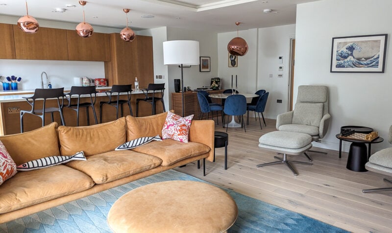 interior of 4 The Reach holiday apartment in Salcombe with a long brown leather sofa and circular leather footstool on a blue rug.