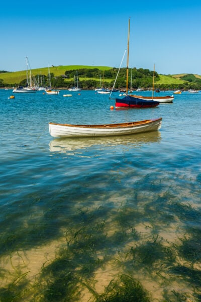 white wooden boat in a river with seagrass visible below the very clear water and a green hill in the background