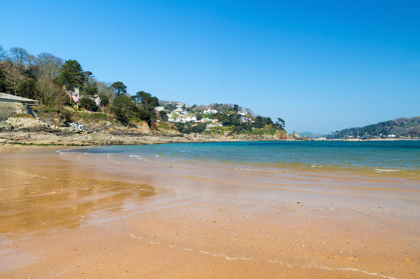 Golden sandy beach with very blue sea and a small hill behind with white hosues at South Sands Salcombe South Hams Devon England