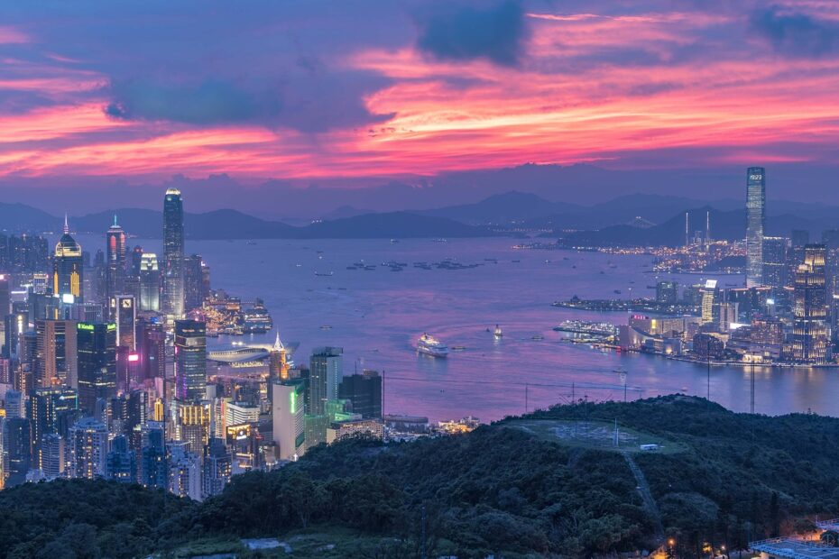 hong kong city seen from above next to ocean at dawn with many skyscrapers lit up and a purple and pink sky overhead