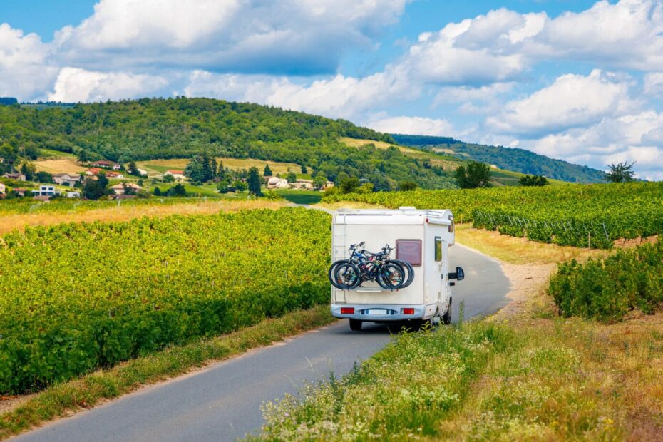 Motorhome driving on a country road next to a vineyard on a sunny day in France.