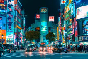city street in tokyo at night awith a buys road surrounded by tll buildings covered with led billboards