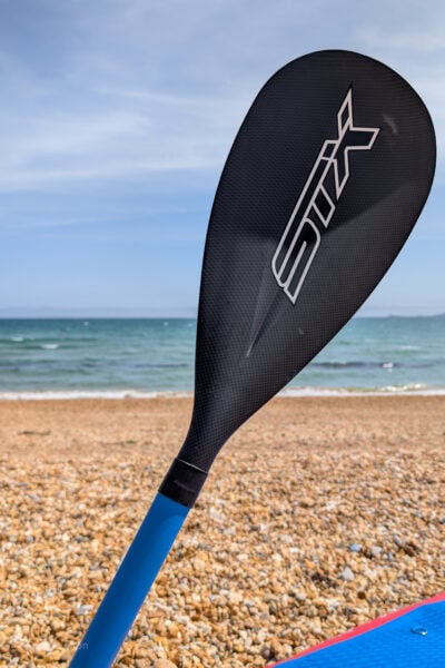 Black paddle in front of a stony beach with the sea