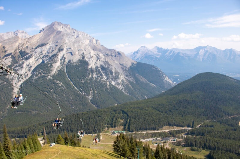 Ski chairlift in summer with grass and trees below and a mountain behind in