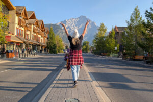 Emily walking in the centre of a street in Banff with her arms in the air and a mountain behind