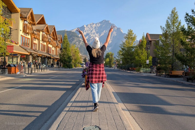 Emily walking in the centre of a street in Banff with her arms in the air and a mountain behind | My Canada Trips review