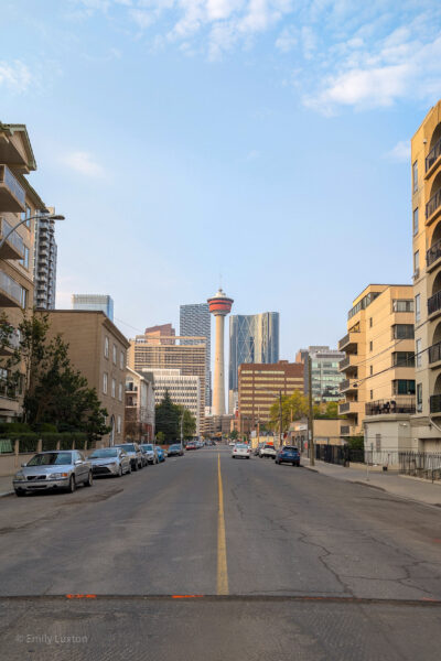 Looking down a road in a city with buildings either side and the Calgary Tower in the distance
