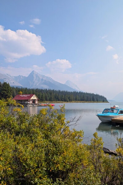 Blue lake with a small boat in the foreground and a red wooden boathouse in the distance