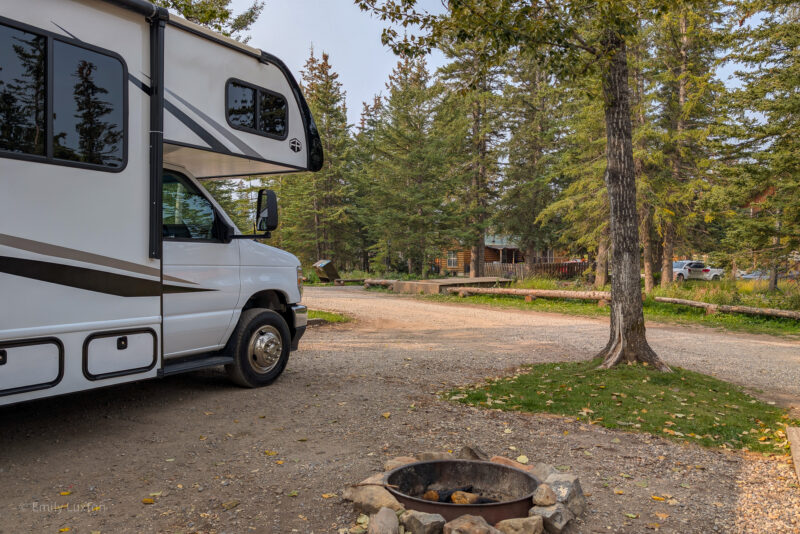 Large white motorhome parked next to a plot with a firepit and