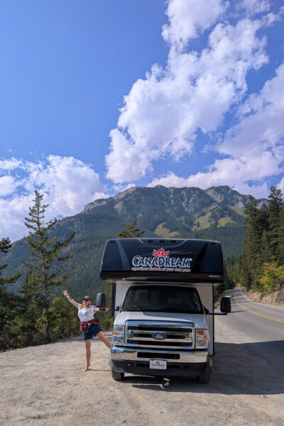 Emily leaning out of the door of a large CanaDream motorhome parked at the side of a road with a mountain behind | My Canada Trips review