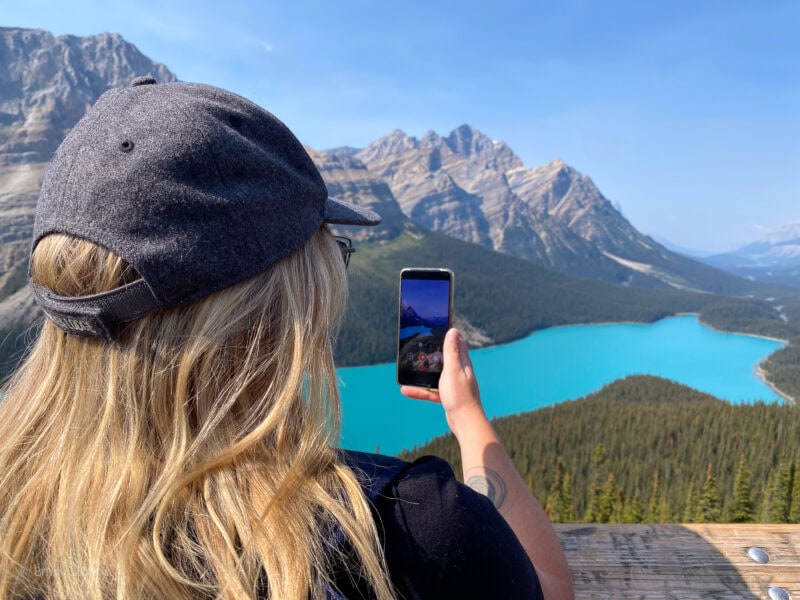 Emily viewed from behind taking a photo on her phone of a very bright blue lake