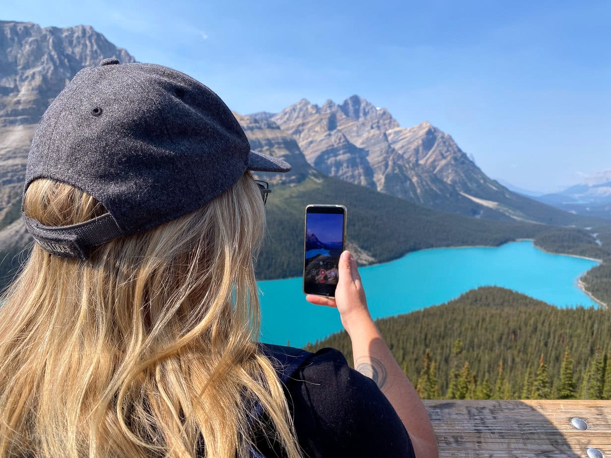 Emily viewed from behind taking a photo on her phone of a very bright blue lake