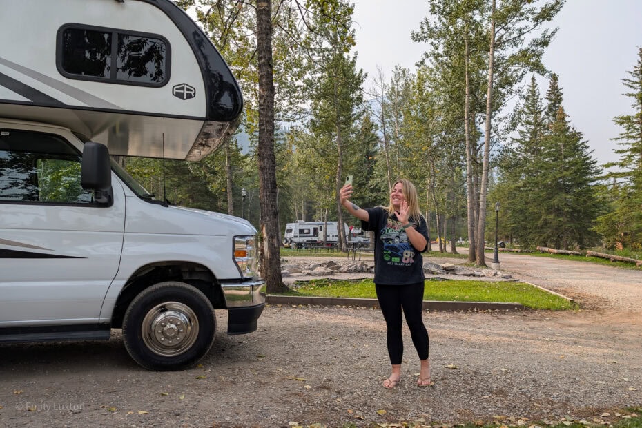 Emily standing next to a white RV talking into her phone and waving