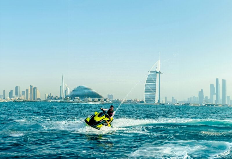 man riding a neon green jet ski in the sea with Dubai skyline behind