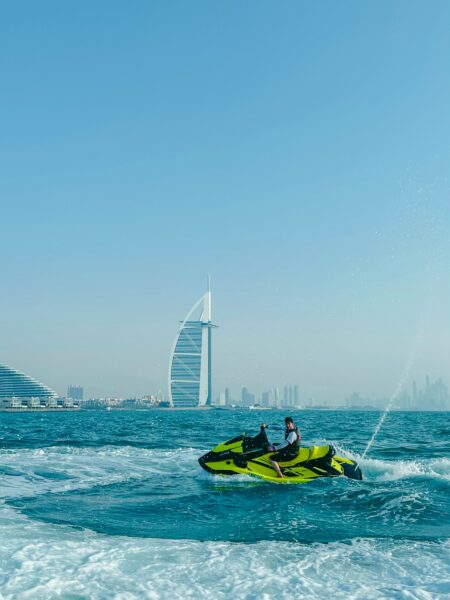 man riding a neon green jet ski in the sea with Dubai skyline behind
