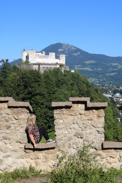 emily sitting on a stone wall with a view of a hilltop castle 