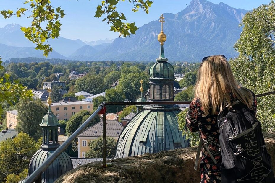 Emily taking a photo of Salzburg skyline with a green dome in front of her and mountains in the background