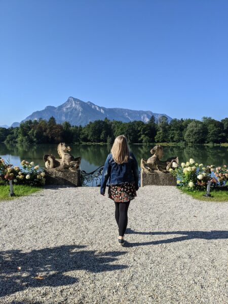 emily wearing a blue denim jacket walking towards a lake with a mountain on the far side