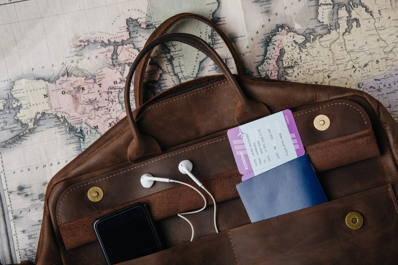 How to Take Care of Your Documents During Your Trip (Including DIY Passport Photos) top view of leather bag with passport, ticket, smartphone and earphones on map
