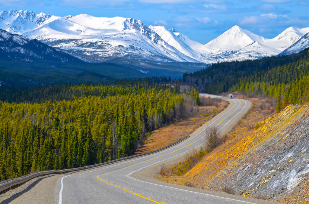 Aerial view of the Alaska Highway in the Yukon, Canada, with snow covered mountains and conifer woods.