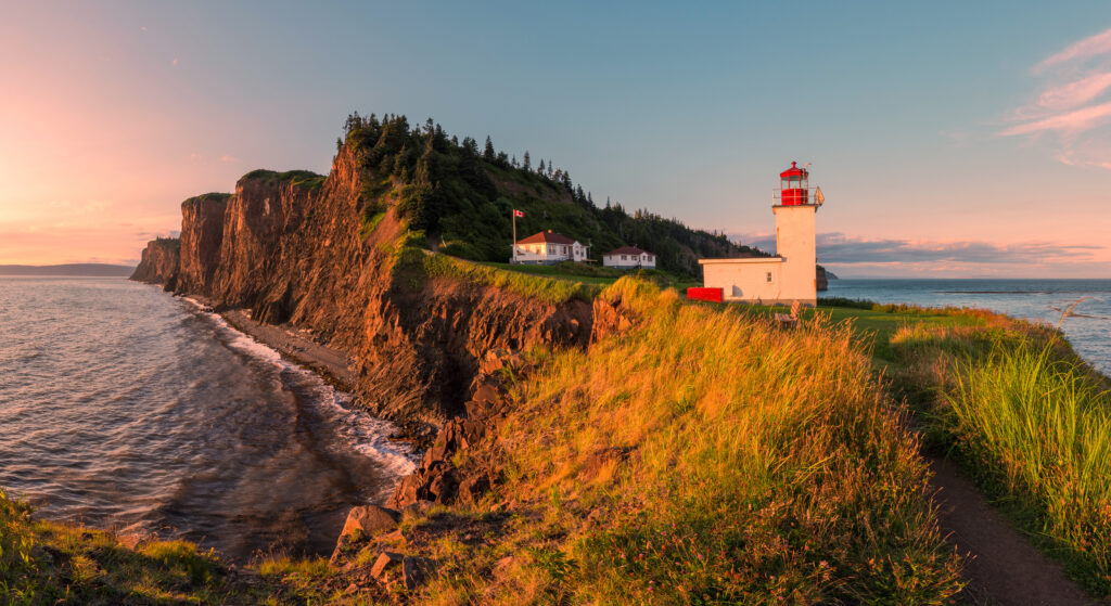Grassy headland with rocky cliffs topped by a white and red lighthouse
