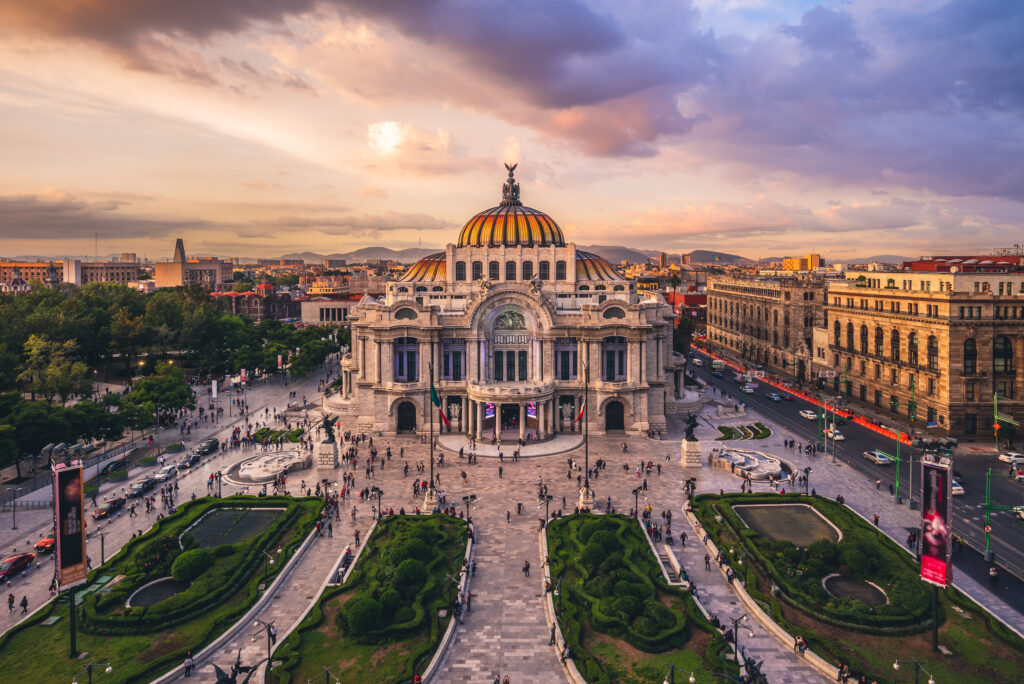 aerial view of a palace style building with a park in front in Mexico City art dusk