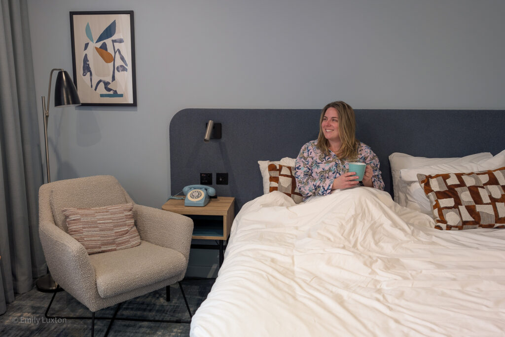 emily sitting in a bed with pink pyjamas on holding a coffee mug