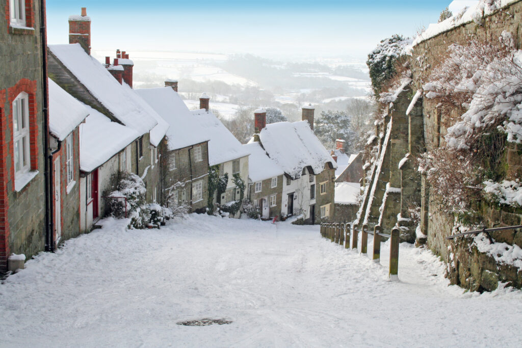 street covered in snow with stone cottages in a line on the left running down the hill