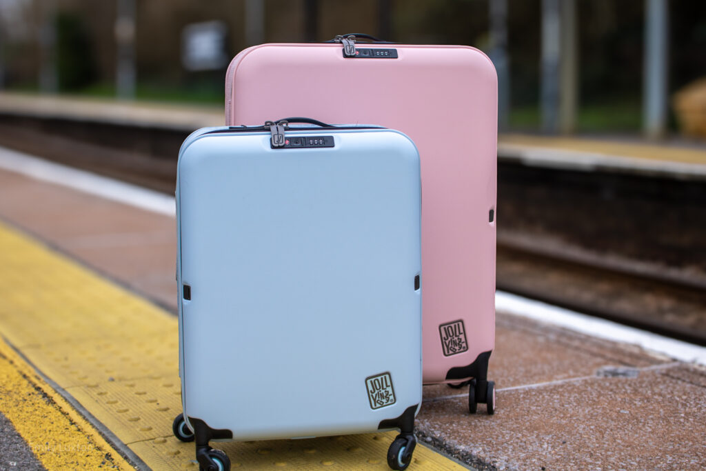 A large pink and small blue hardshell suitcase on a train station platform | JOLLYING Pebble Review