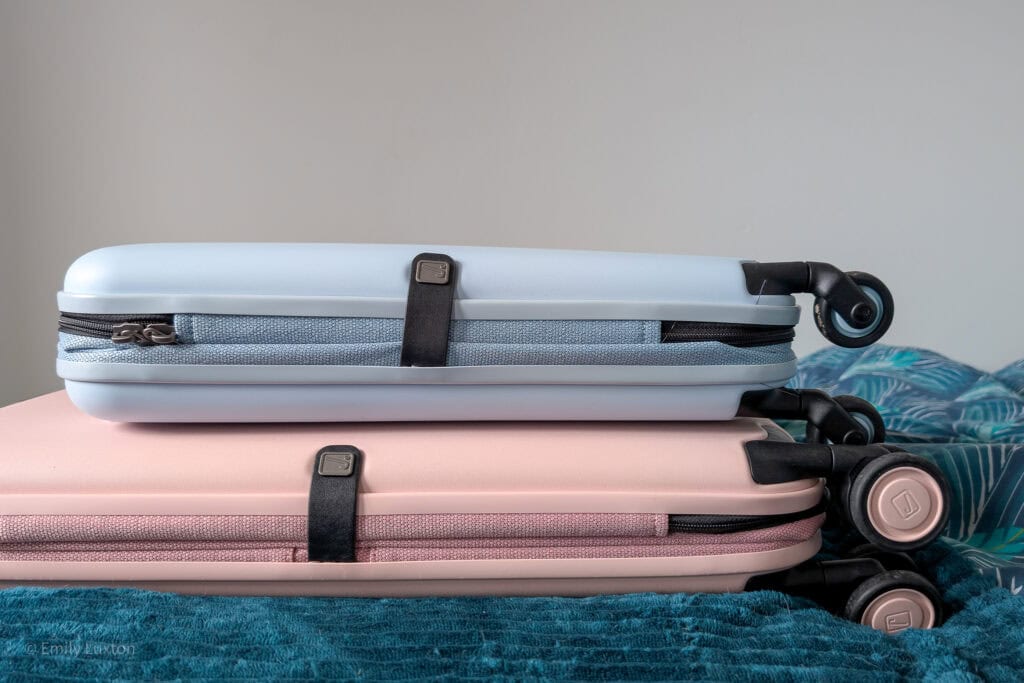 A large pink and small blue hardshell suitcase collapsed to half original width on a bed