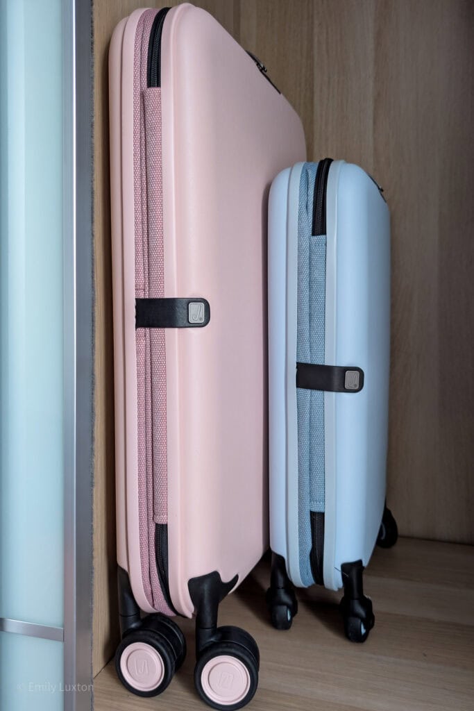 A large pink and small blue hardshell suitcase collapsed to half original width inside a wardrobe