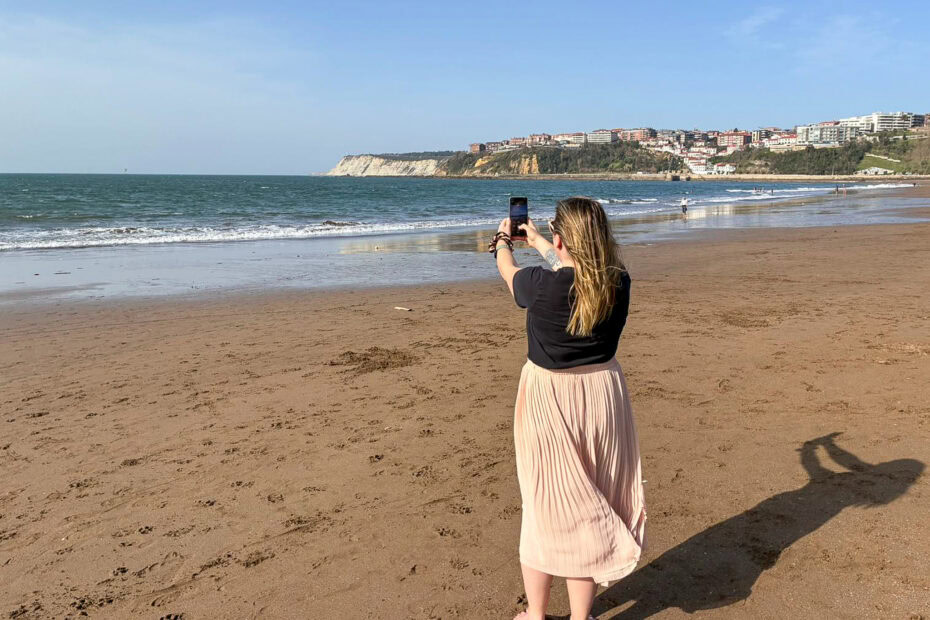 emily on a beach wearing pink skirt and black t-shirt taking a photo with her phone