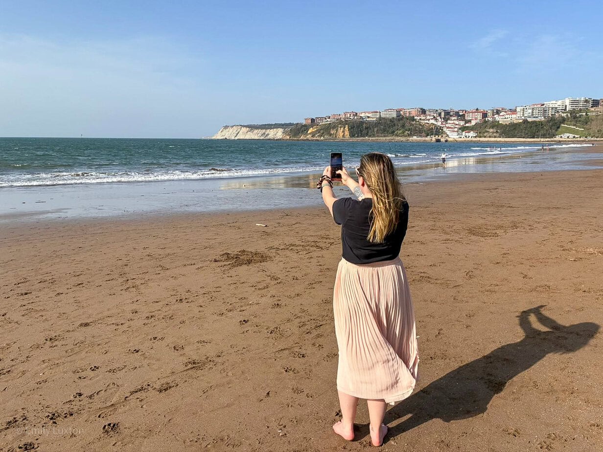 emily on a beach wearing pink skirt and black t-shirt taking a photo with her phone