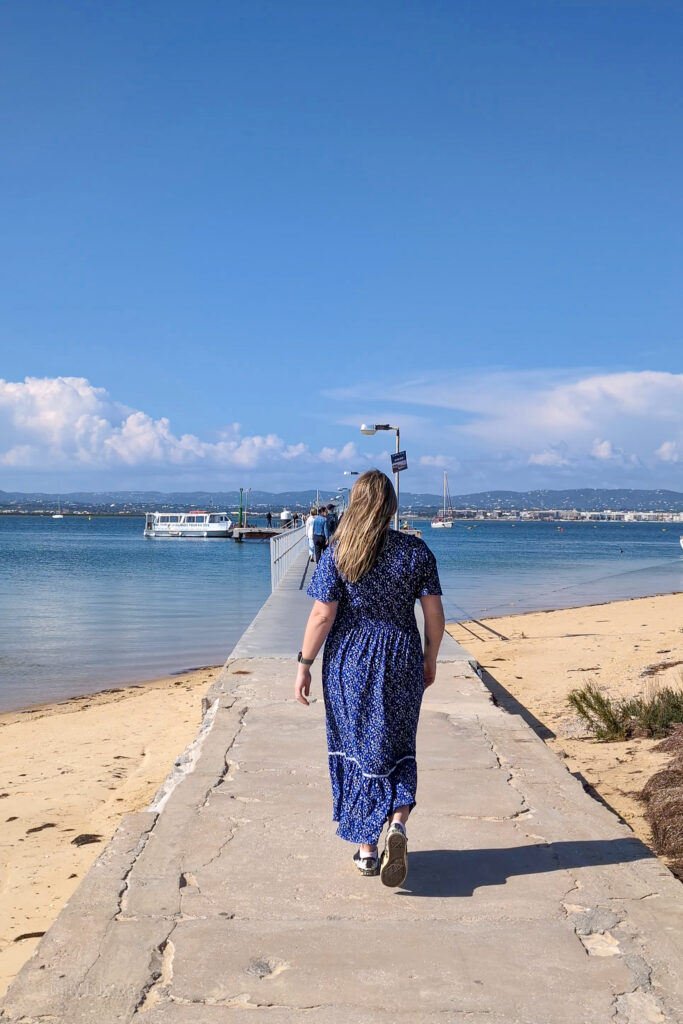 emily wearing a long blue dress walking along a jetty towards a small white boat
