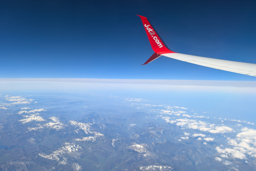 Plane wing with red tip and Jet2 logo with clouds and snowy mountains below | 3 days in the algarve