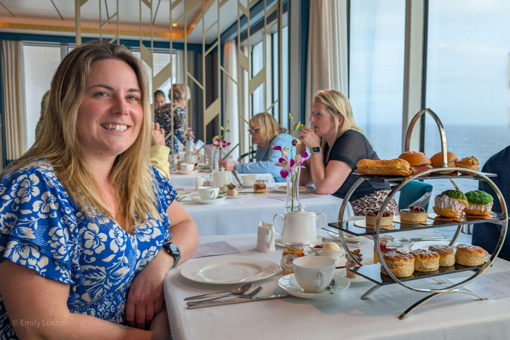 Emily in a blue dress at a table with a white tablecloth and afternoon tea on a 3-tier cake stand | P&O Iona Speciality Restaurants