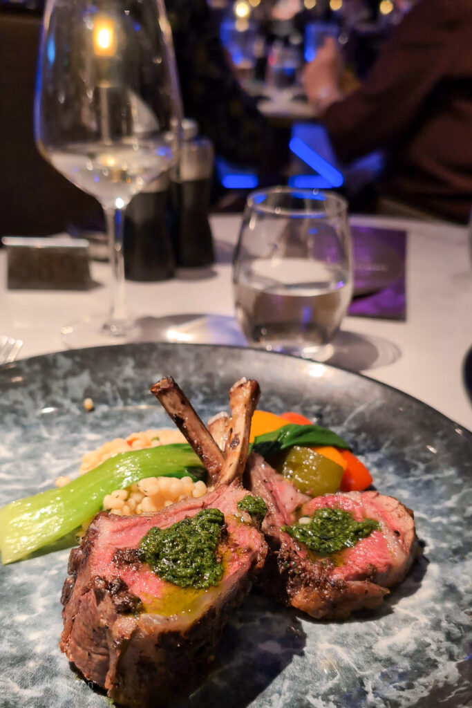 Two lamb cutlets on a blue plate with a glass of wine alongside