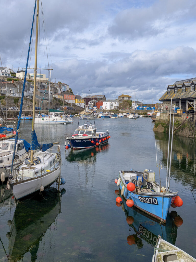 Fishing boats in Mevagissey harbour with a stone wall and a village behind