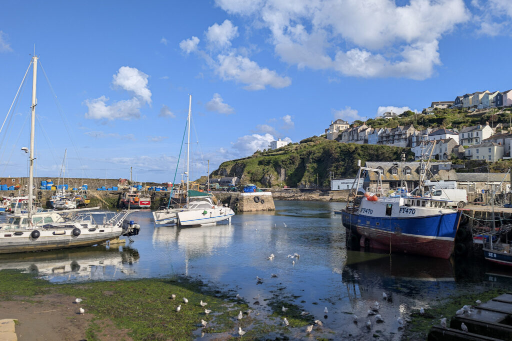 Fishing boats in Mevagissey harbour with grey stone wall and a grassy hill behind