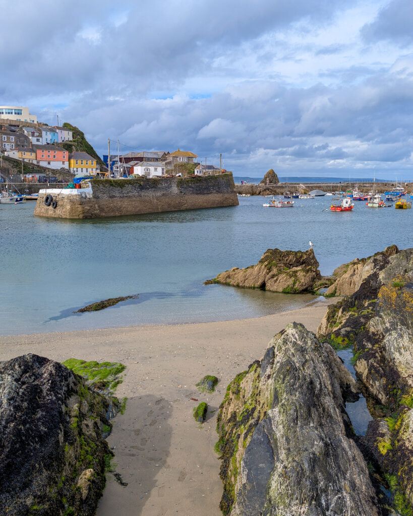 small sandy beach with rocks next to a harbour with stone walls