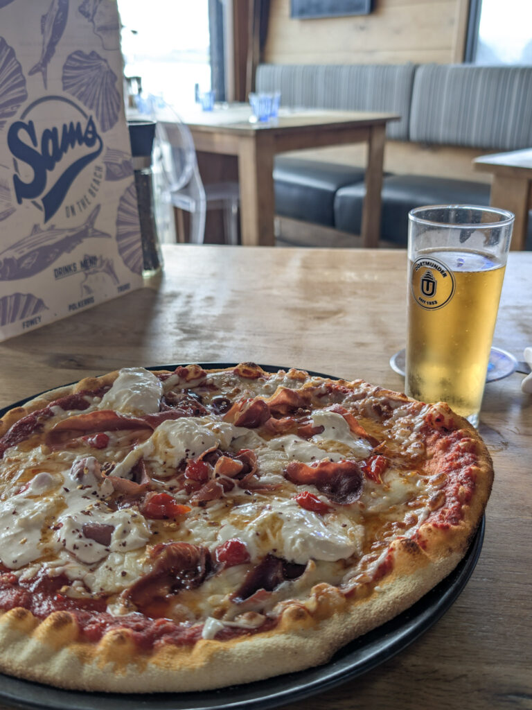Pizza and half pint of beer on a wooden table