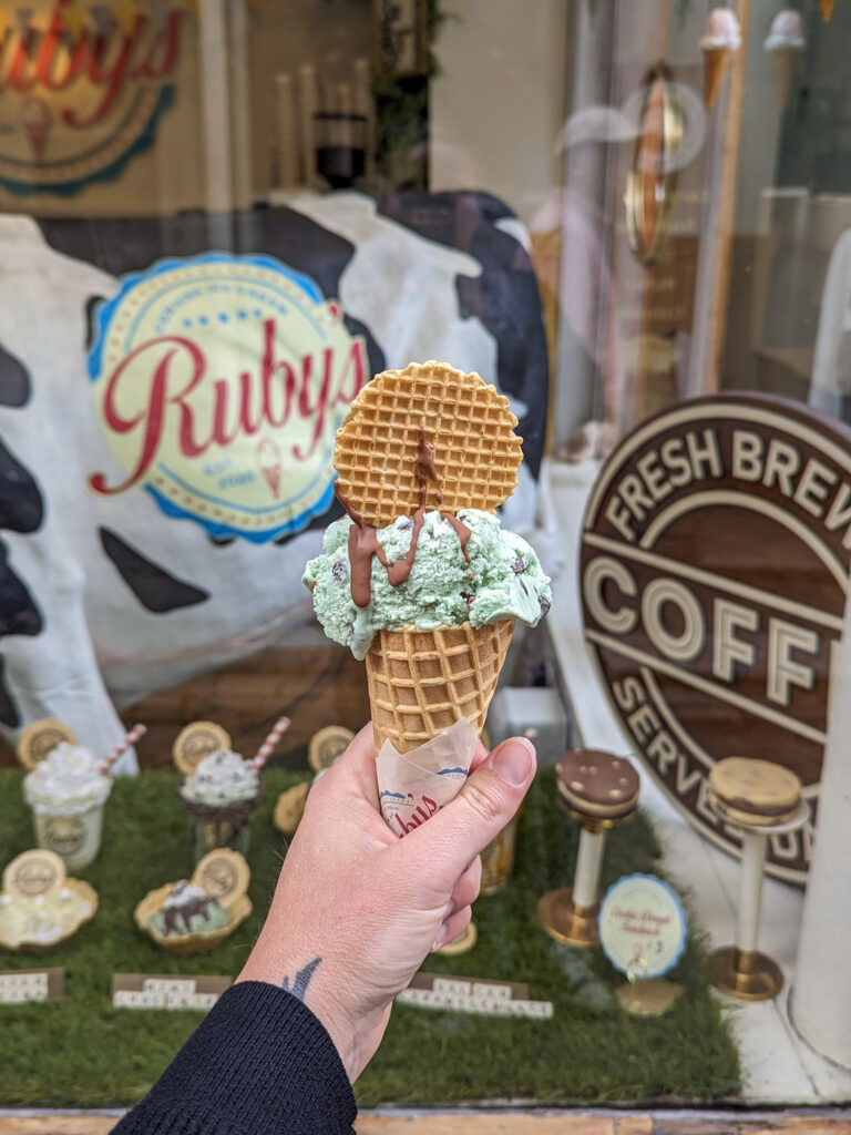 Hand holding an ice cream cone with a waffle on top and chocolate sauce