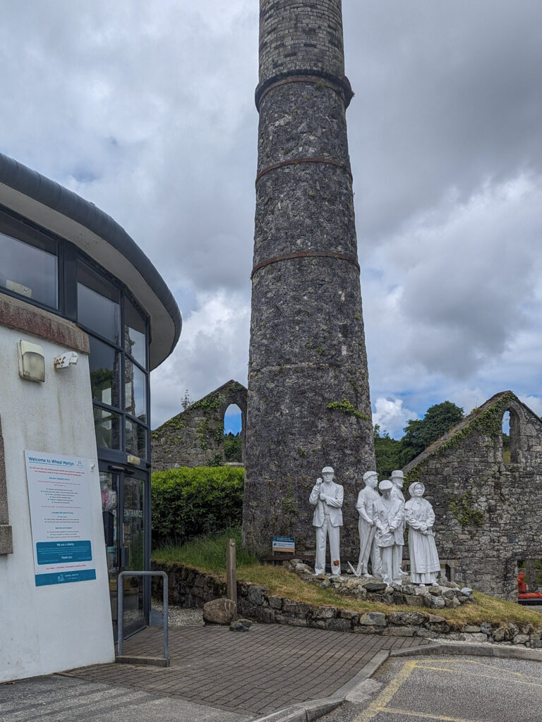 White china statue of miners in front of a tall grey stone chimney 