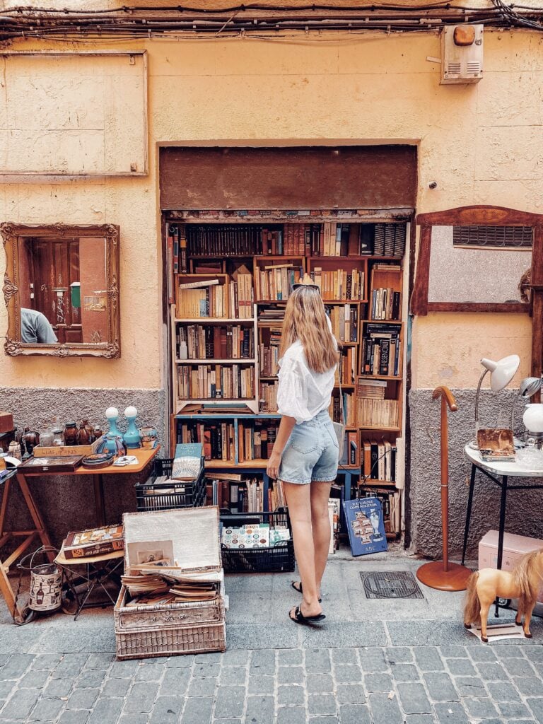 Girl in denim shorts and white top browsing a bookshelf at a market