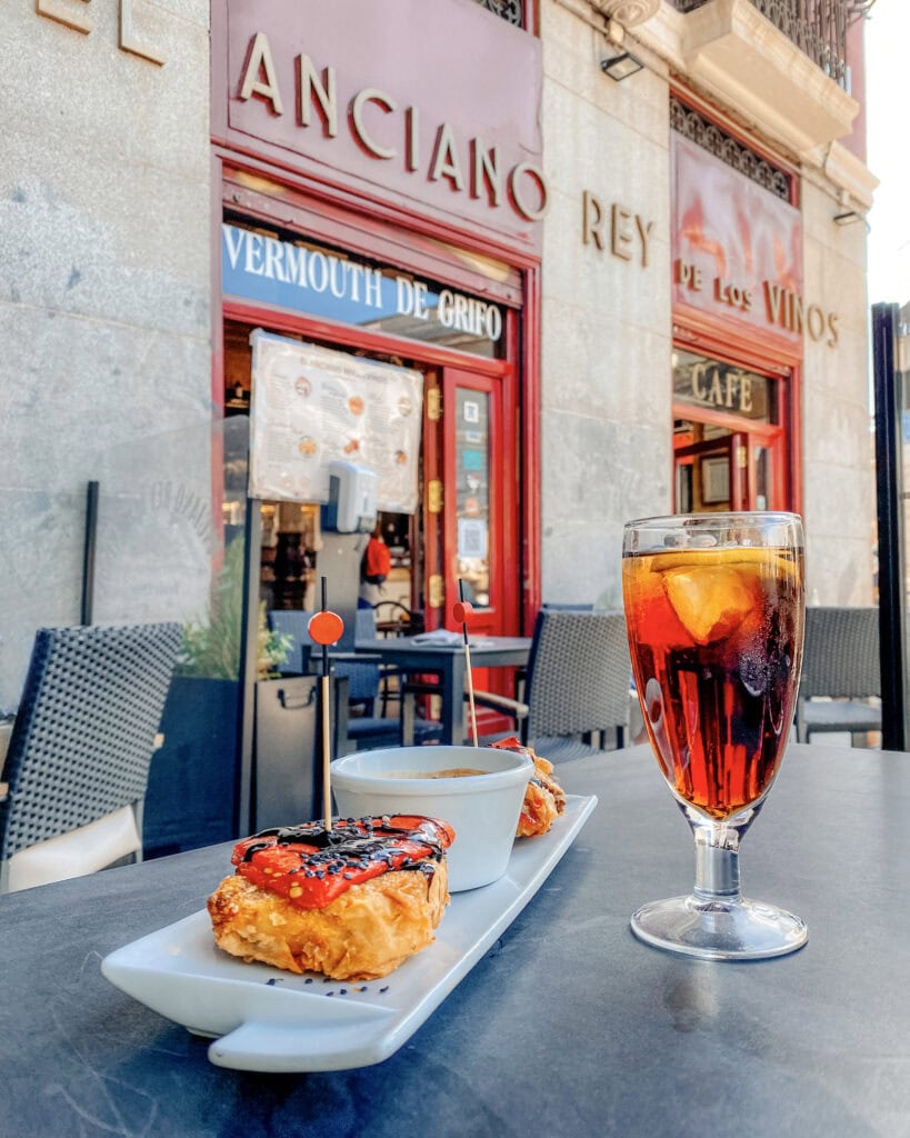 glass of sangria and plate with small tapas dish on a table outside a bar