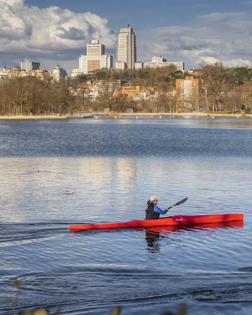 Person on a red kayak in a late with Madrid city skyline behind