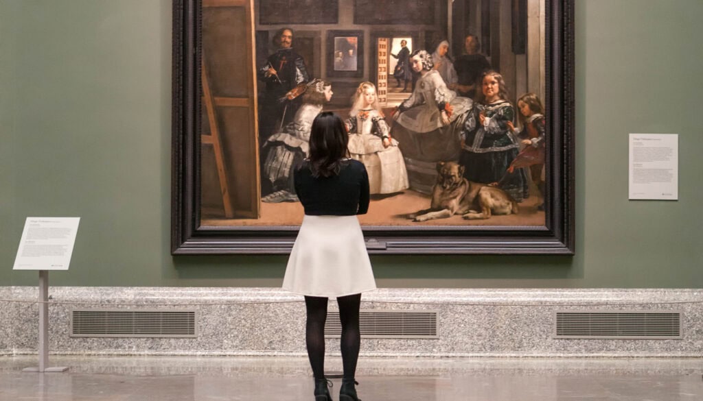 Girl in a white skirt and black top looking at a painting in the Museo del Prado in Madrid
