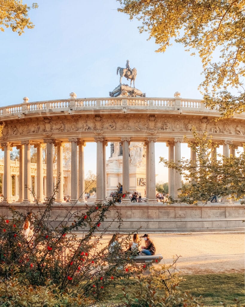 3 people sitting on a bench in front of the rotunda in Retiro Park madrid 